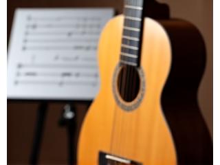 En akustisk gitar i fokus, med et notestativ i bakgrunnen.